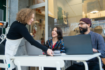 A woman serving coffee to another woman and a man A woman serving coffee to another woman and a man