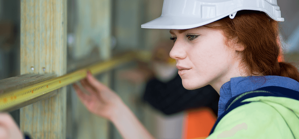 Female apprentice wearing hardhat measuring wall