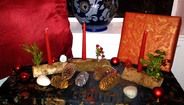 Wooden candle holders with red candles and branches of winter berries, presented with colourful festive pinecones and baubles