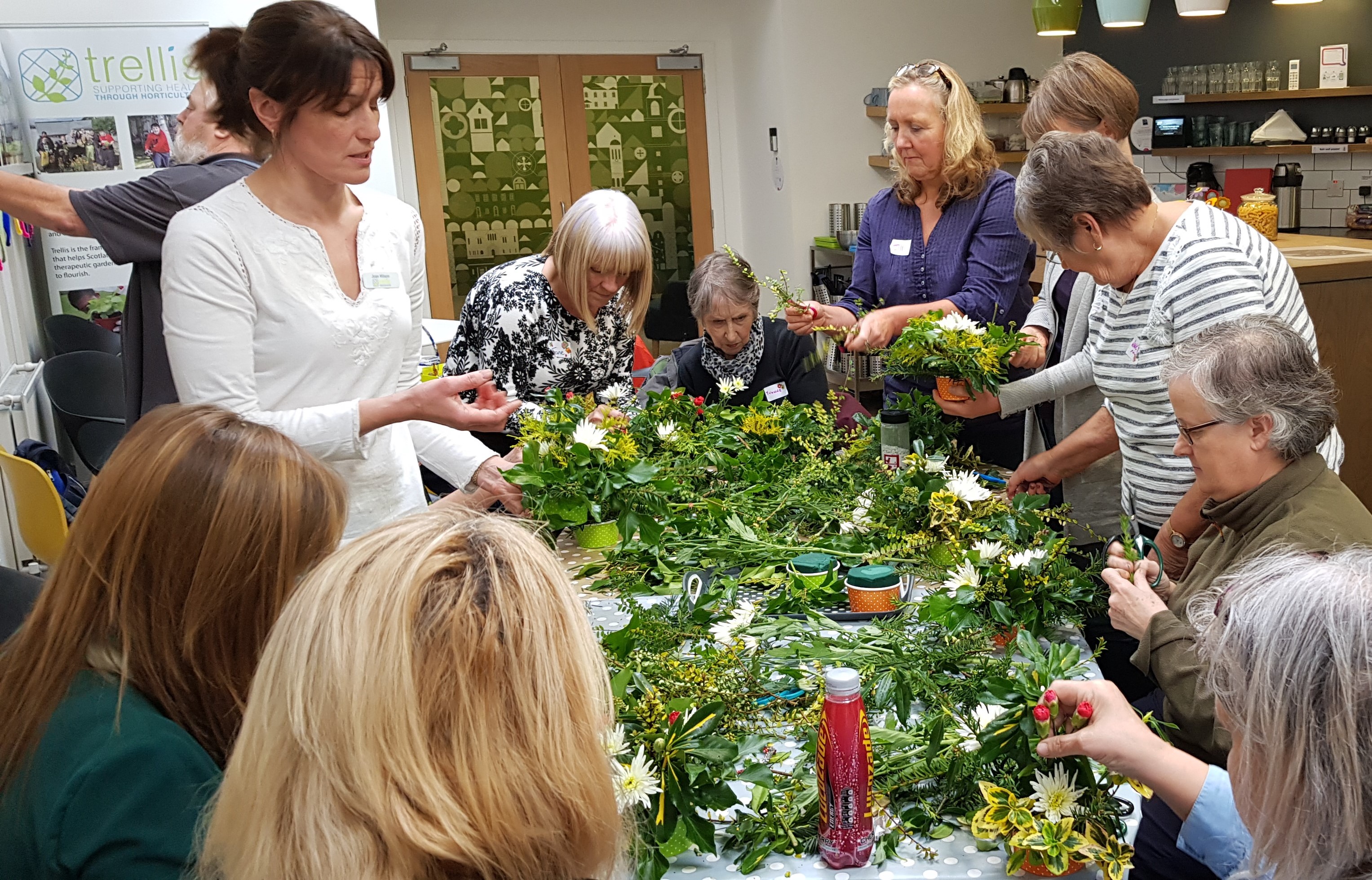 A group of ladies sat around a table doing flower arranging with Trellis