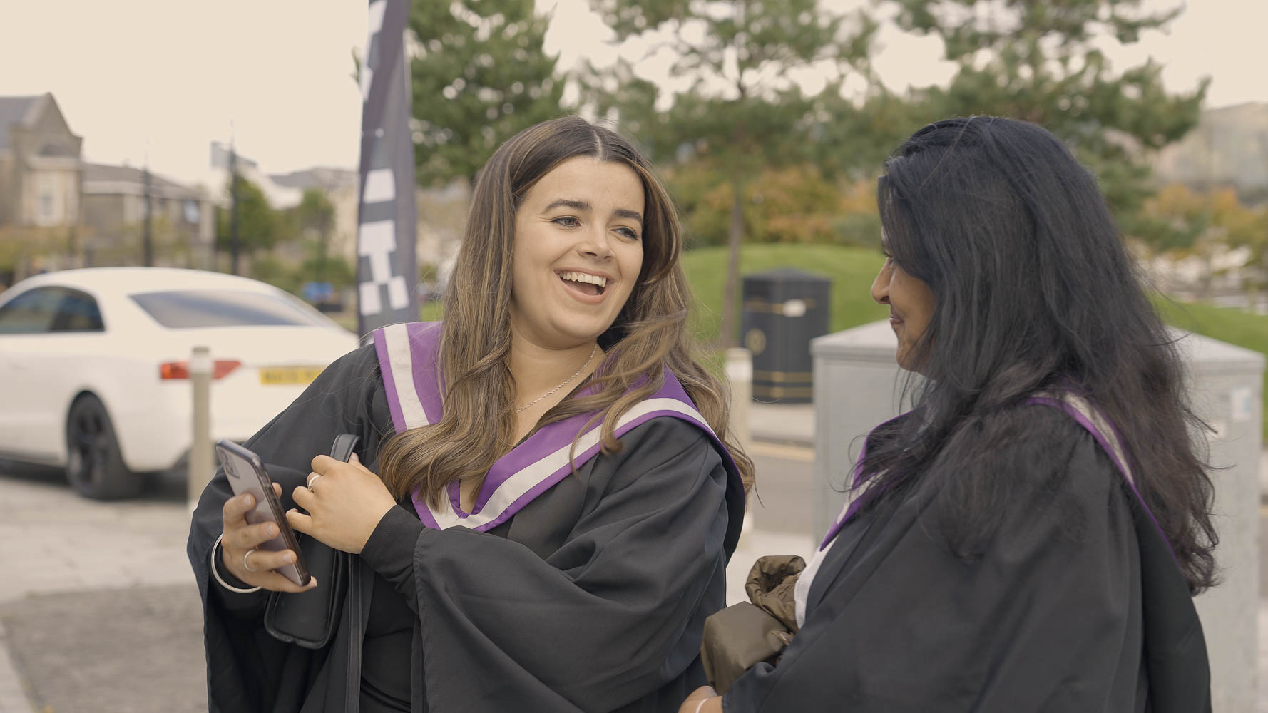 Two students dressed in academic robes outside the graduation venue Two students dressed in academic robes outside the graduation venue