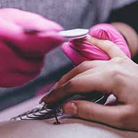 Nail technician wearing PPE buffing the nails of a client