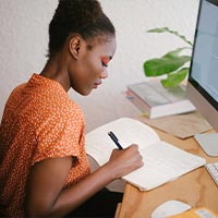 Woman making notes at her desk, with computer screen on in front of her