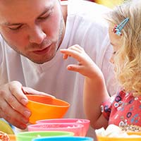 Male childcare practitioner and young girl playing with colourful cups