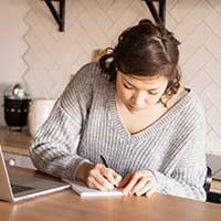 Woman writing notes next to laptop